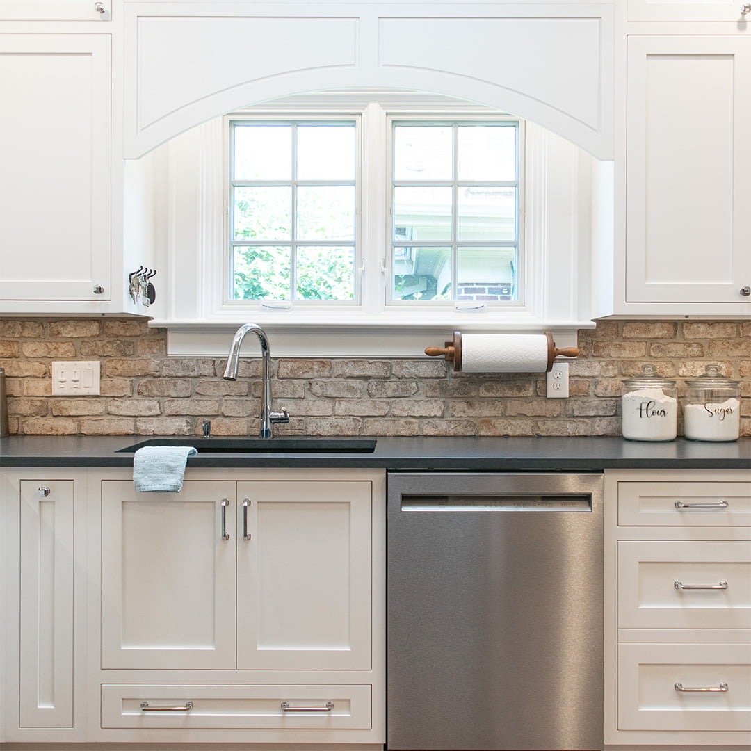 white kitchen cabinets with dark countertop and brick backsplash