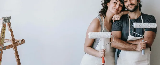 young couple smiling holding paint rollers during kitchen remodel